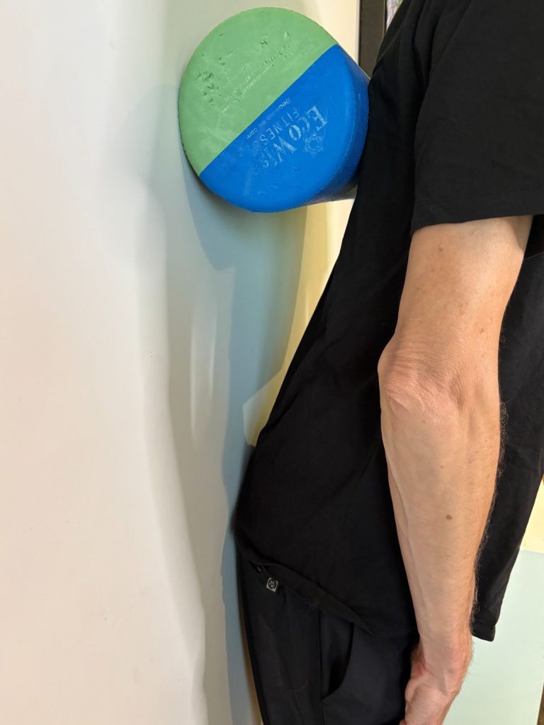 Patient pushing hips gently back toward wall to correct forward pelvic shift in swayback posture.