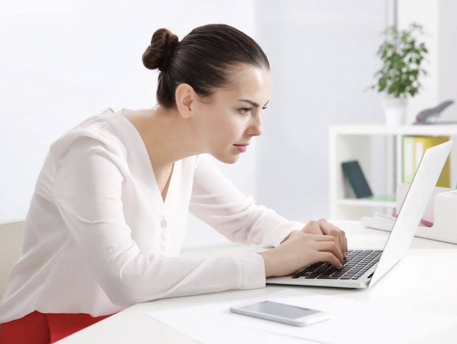 Woman leaning forward at a laptop with poor posture, a common cause of neck-related headaches and neck pain.